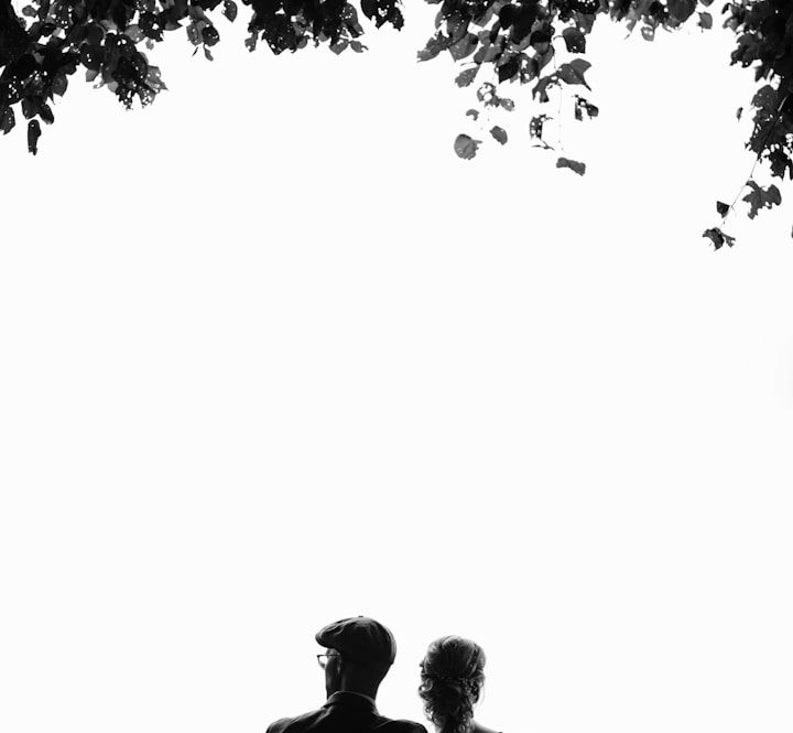 Zwei Personen nebeneinander unter Bäumen, silhouettiert vor hellem Hintergrund.