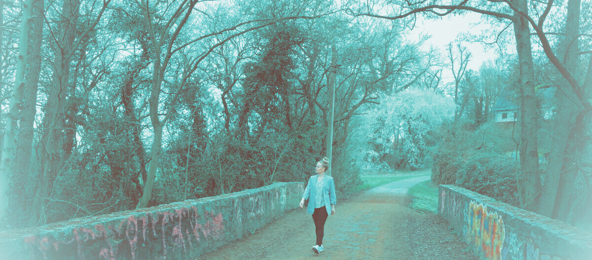 Psychologische Beraterin Sonja Schüssele geht allein über eine Brücke, umgeben von Bäumen und Graffiti. Beratung in Darmstadt.